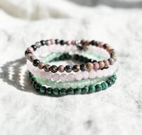 a stack of bracelets with pink, green, and black stones