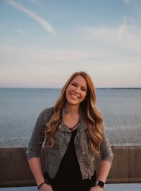 a young woman sitting on a wall next to the ocean